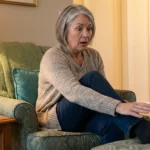 Woman with neuropathy reacting to sudden electric shock sensation in foot while sitting at home