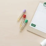 Editorial flat-lay of blood draw vials, a clipboard, and a generic dental hygiene tube — illustrating copper deficiency neuropathy causes and diagnosis.