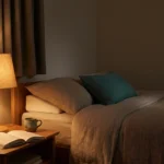 A calm dimly-lit bedroom at night with a soft bedside lamp, paper book, and water — a restful setting for sleeping with neuropathy.