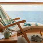 A serene ship balcony with a deck chair, blanket, cruise itinerary, supportive shoes, and tea — anchoring the calm of a well-planned neuropathy cruise.