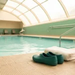 Calm community pool deck with closed-toe water shoes, towel, and water bottle ready for a safe neuropathy-friendly swim session