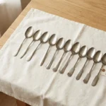 Twelve simple silver teaspoons arranged in a row representing the Spoon Theory daily energy budget