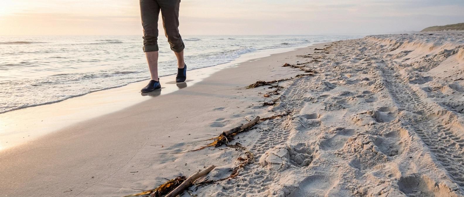 Beach with visible difference between soft dry sand and firm wet packed sand at the tide line where a person walks in water shoes
