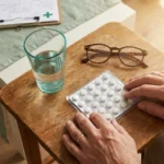 Unlabeled white pills in blister pack on wooden table with water glass — investigational diabetic neuropathy medication