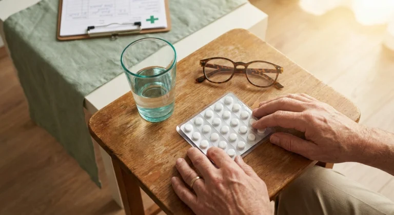Unlabeled white pills in blister pack on wooden table with water glass — investigational diabetic neuropathy medication