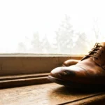 Worn leather shoe on a windowsill with a raised bulge across the toe box