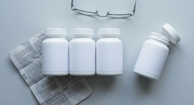 Four unlabelled pill bottles in a row on a grey desk, one pushed aside with its cap off
