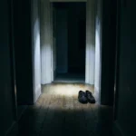 Dark hallway lit by a single head torch beam with shoes on the floor ahead