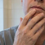 A person touching their own lower lip and chin, seen close and cropped below the eyes