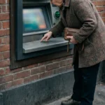 Older woman pressing keys at an outdoor ATM set in a brick wall
